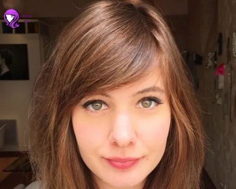 A woman with side-swept bangs styled to frame her face elegantly, paired with shoulder-length hair.