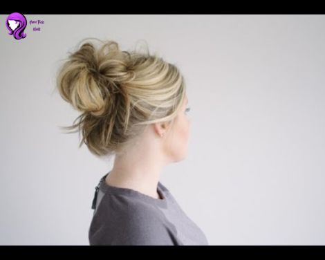 A casual messy bun hairstyle with loose strands framing a woman's face for a youthful vibe.