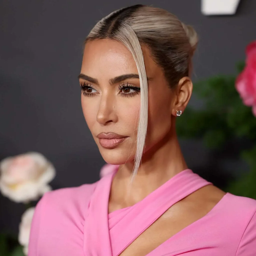 Kim Kardashian’s sleek middle-part low bun, shiny finish, professional hair styling.